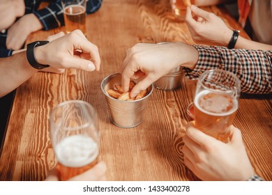 Beer and snacks crackers, croutons with sauce. Men in pub bar behind wooden table.