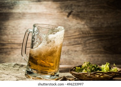 Beer spills from cup on wooden table next to hop in basket