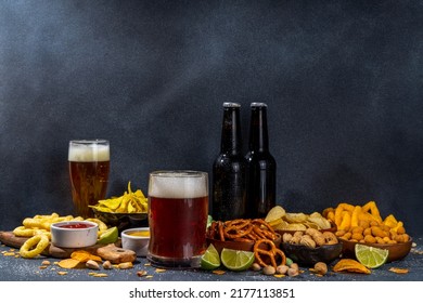 Beer with various salted snacks set. Black table background with traditional party snacks, beer bottles and glasses, with chips, onion rings, salted nuts, crisps and sauces top view copy space - Powered by Shutterstock