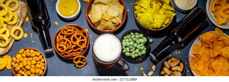 Beer With Various Salted Snacks Set. Black Table Background With Traditional Party Snacks, Beer Bottles And Glasses, With Chips, Onion Rings, Salted Nuts, Crisps And Sauces Top View Copy Space