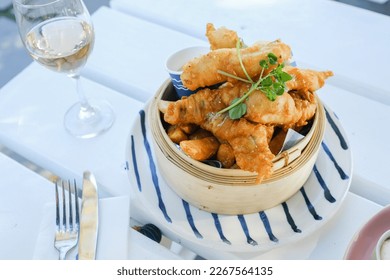 Beer-battered flathead and garlic aioli, served in a bamboo steamer on a striped plate with a glass of rosé wine at a café in Palm Beach, Sydney, New South Wales, Australia