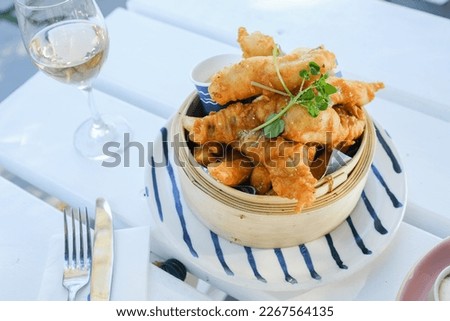 Beer-battered flathead and garlic aioli, served in a bamboo steamer on a striped plate with a glass of rosé wine at a café in Palm Beach, Sydney, New South Wales, Australia