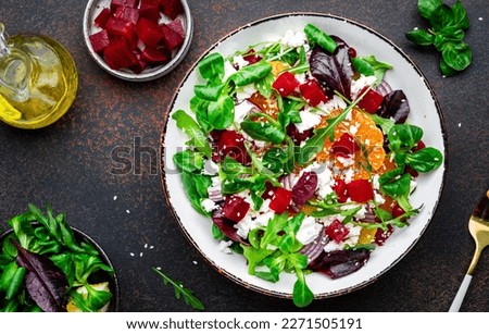 Beet, cheese and orange healthy salad with arugula, lamb lettuce, red onion, walnut and tangerine, brown kitchen table. Fresh useful dish for healthy eating