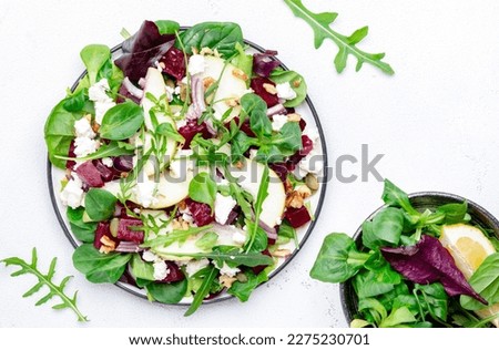 Beet, feta cheese and pear healthy salad with arugula, lamb lettuce, red onion, chard and walnut, white kitchen table. Fresh delicious dish for healthy eating