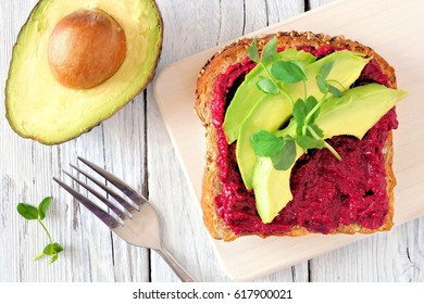 Beet hummus and avocado toast with pea shoots on server, top view on white wood background