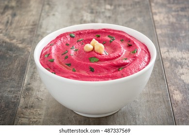 Beet hummus in a bowl on wooden table background

