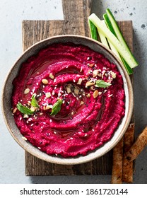 beet hummus in a ceramic bowl on a wooden cutting board, top view