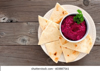 Beet hummus dip with pita bread on a plate, above view on a rustic wooden background