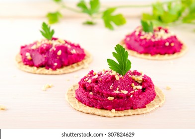 Beet hummus with peanuts and parsley on thin wafers.