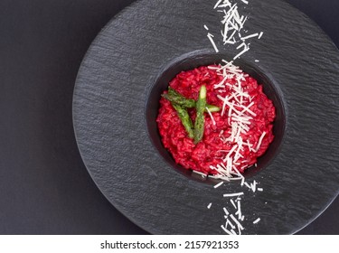 Beet risotto with asparagus and a strip of grated parmesan cheese on the black plate 