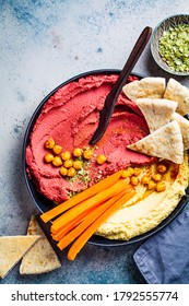 Beetroot and classic hummus in black dish with carrots and pita bread.