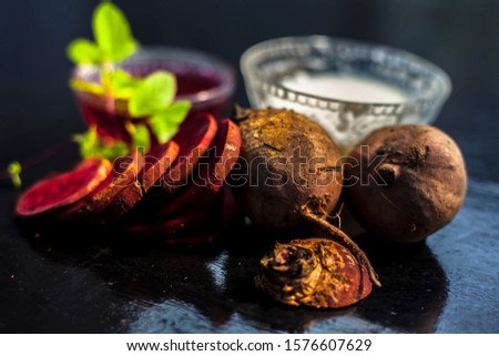 Beetroot face mask on the black glossy surface consisting of some grated beetroot vegetable and sour cream well mixed in a glass bowl along with raw cut sliced beetroot vegetable and cream.
