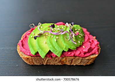 Beetroot hummus and avocado open face sandwich with radish sprouts. Isolated,black background
