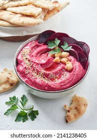 beetroot hummus in a bowl garnished with sesame seeds, beet slices, chickpeas, parsley and olive oil. Served with pita bread.