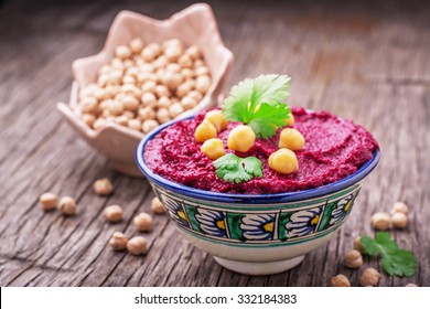Beetroot hummus with chickpeas and cilantro sprigs in a blue painted bowl on dark wooden background. selective Focus