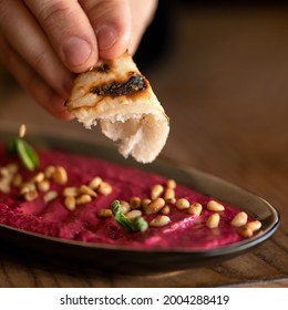 Beetroot Red Puree With Peanuts. Male Hand Dipping Piece Of Pita Bread Into Bowl With Beetroot Hummus Or Dipping Sauce. Close-up Shot. Soft Focus. Copy Space.