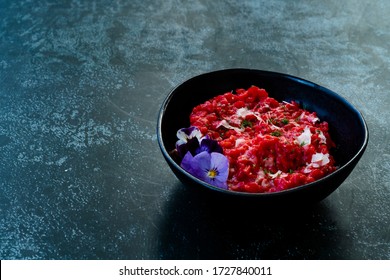 Beetroot Risotto with Edible Flowers and Parmesan Cheese made with Organic Beet in Black Ceramic Bowl. Healthy Organic Food.