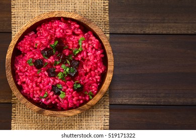 Beetroot risotto prepared with beetroot puree, roasted beetroot pieces and parsley on the top, photographed overhead on dark wood with natural light (Selective Focus, Focus on the top of the risotto)