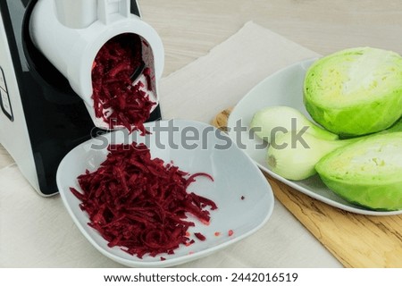 Beets, onion and cabbage in a vegetable cutter on kitchen table. Chopped beet is falling into a bowl. Homemade healthy food. Healthline.