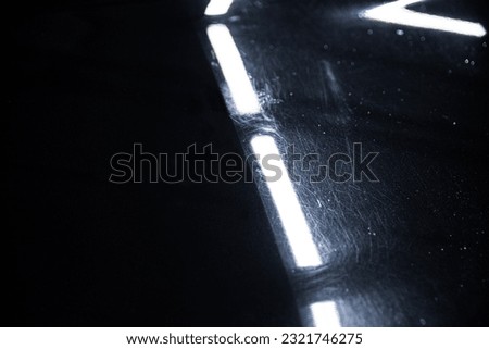 Before and after effect of a paint correction on the paintwork of a black car in a car detailing studio.