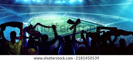 Before match. Back view of football, soccer fans cheering their team with and scarfs at crowded stadium at evening time. Concept of sport, cup, world, team, event, competition. Blue light