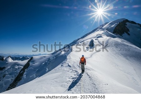 Before Mont Blanc (Monte Bianco) summit 4808m last ascending. Team roping up Man with climbing axe dressed high altitude mountaineering clothes with backpack walking by snowy slopes with blue sky.