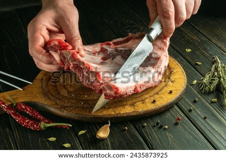 Before preparing a meat dish, the chef cuts raw ribs with a knife on a cutting board. Low key recipe idea for saloon.