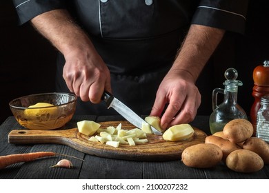 Before Preparing The National Dish, The Chef Cuts Raw Potatoes Into Small Pieces With A Knife. Close-up Of A Cook Hands While Working In A Restaurant Kitchen.