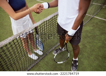 Before the start of tennis match, two opponents approached the net on the tennis court to shake hands. Boy and girl are holding rackets, wearing sneakers and shaking hands.