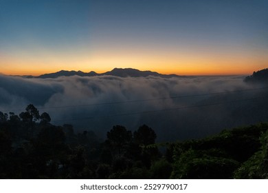 Before sunrise view, painted sky with soft orange light in the horizon. Dense clouds covers the valley and mountains in background above the clouds. Magical morning scene in mountain village in India. - Powered by Shutterstock