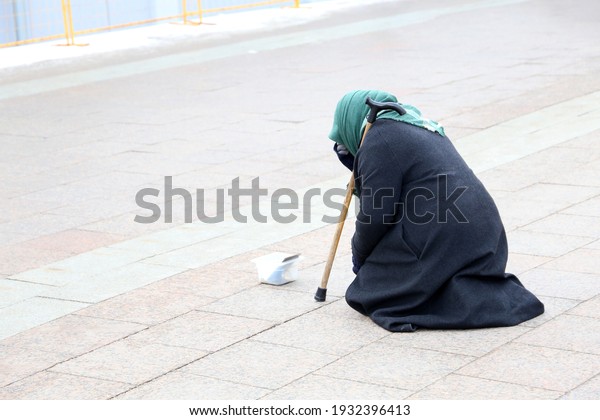 Beggar old woman asks for alms\
sitting on a city street. Poverty, homeless and begging\
concept