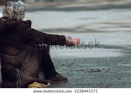 A beggar sits on the street and asks for money
