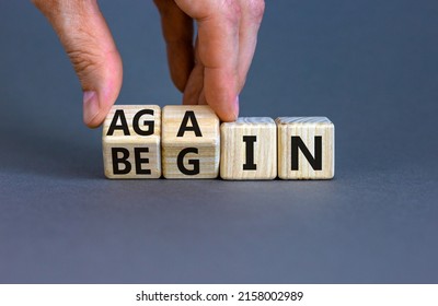 Begin again symbol. Businessman turns wooden cubes and changes the word begin to again. Beautiful grey table, grey background. Business and begin again concept. Copy space.