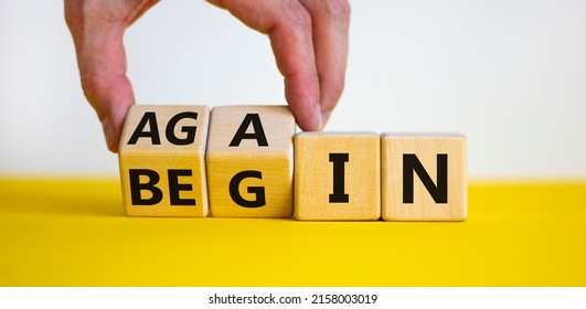 Begin again symbol. Businessman turns wooden cubes and changes the word begin to again. Beautiful yellow table, white background. Business and begin again concept. Copy space.