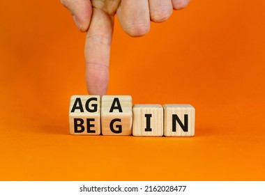 Begin again symbol. Businessman turns wooden cubes and changes the word begin to again. Beautiful orange table, orange background. Business and begin again concept. Copy space.