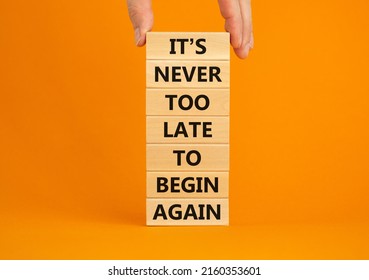 Begin again symbol. Wooden blocks with words 'It is never too late to begin again'. Businessman hand. Beautiful orange background, copy space. Business and It is never too late to begin again concept.