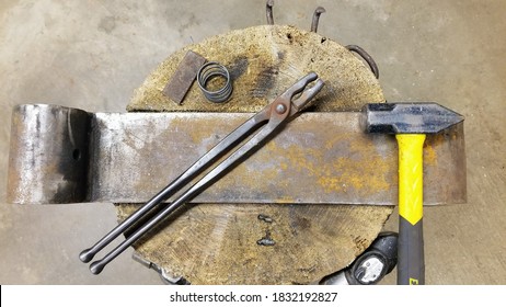 Beginner blacksmith anvil setup (railroad tie in a stump) with wolf jaw tongs and a 3.5 lb. hammer and small steel (a spring and small billet). - Powered by Shutterstock