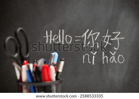 Beginner Chinese language learner writing Hello word Nihao in Chinese characters and pinyin on a chalkboard, concept of learning mandarin