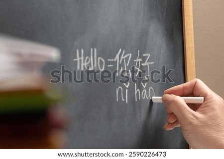 Beginner Chinese language learner writing Hello word Nihao in Chinese characters and pinyin on a chalkboard, concept of learning mandarin