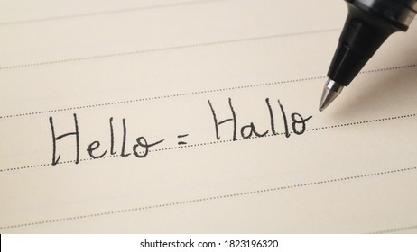 Beginner German or Dutch language learner writing Hello word Hallo for homework on a notebook macro shot