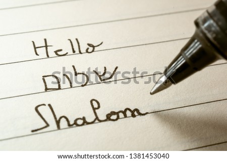 Beginner Hebrew language learner writing Hello Shalom word in Hebrew alphabet on a notebook close-up shot