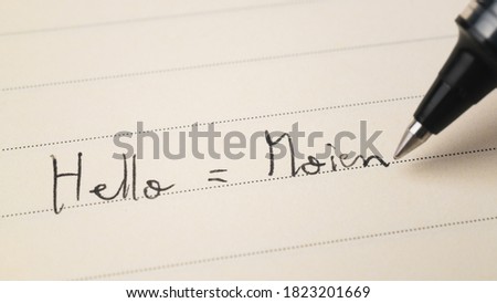 Beginner Luxembourgish language learner writing Hello informal word Moien for homework on a notebook macro shot