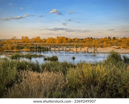 the beginning of the autumn. Autumn landscape with a flowing blue river, yellow trees on the banks and purple clouds on the blue sky. Ilek river, Aktobe, Kazakhstan
