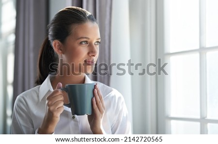 Beginning of the business day. Shot of a young businesswoman enjoying a cup of coffee while standing next to a windown.