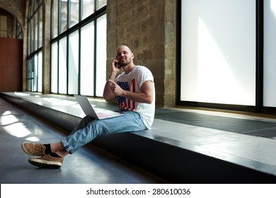 Beginning Business Man Sitting In New Premise For Rent Or Empty Work Space Talking On Mobile Phone,male Interior Designer Or Young Architect Sitting In Empty Office Working On A Laptop And Smart Phone