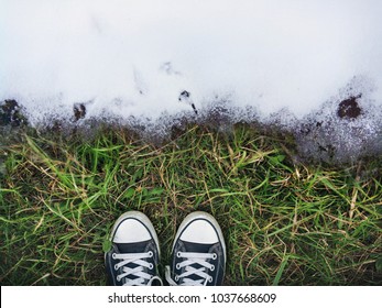 The beginning of spring. The boundary between the grass on the ground and white snow symbolizes the transition from winter to spring or from autumn to winter. Snow is melting. Sneakers on the grass. - Powered by Shutterstock