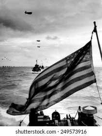 Behind an American flag, a convoy of landing craft head for Utah Beach on June 6, 1944. Each ship has barrage balloon connected by a cable during the D-Day invasion of Normandy on June 6, 1944.