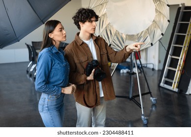 Behind the camera. Dynamic duo in modern photostudio preparing for photo or video shooting, photographer guy working in team with assistant, free space - Powered by Shutterstock