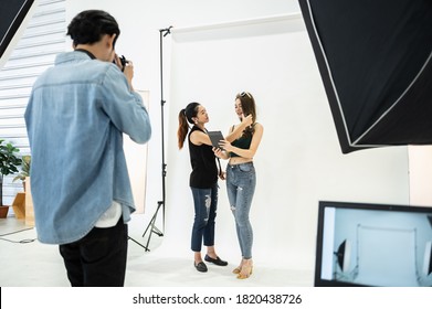 Behind the scene of photo shoot: Asian make-up artist applies makeup on young beautiful model while photographer directions vision creative ideas photoshoot on white background in modern studio.