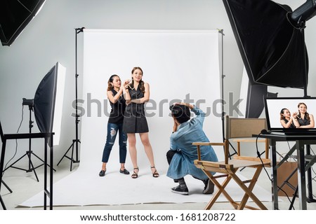 behind the scene of Professional photo shooting at the studio: a beautiful young asian model is smiling and posing with makeup artist is makeup photographer is taking pictures with a digital camera